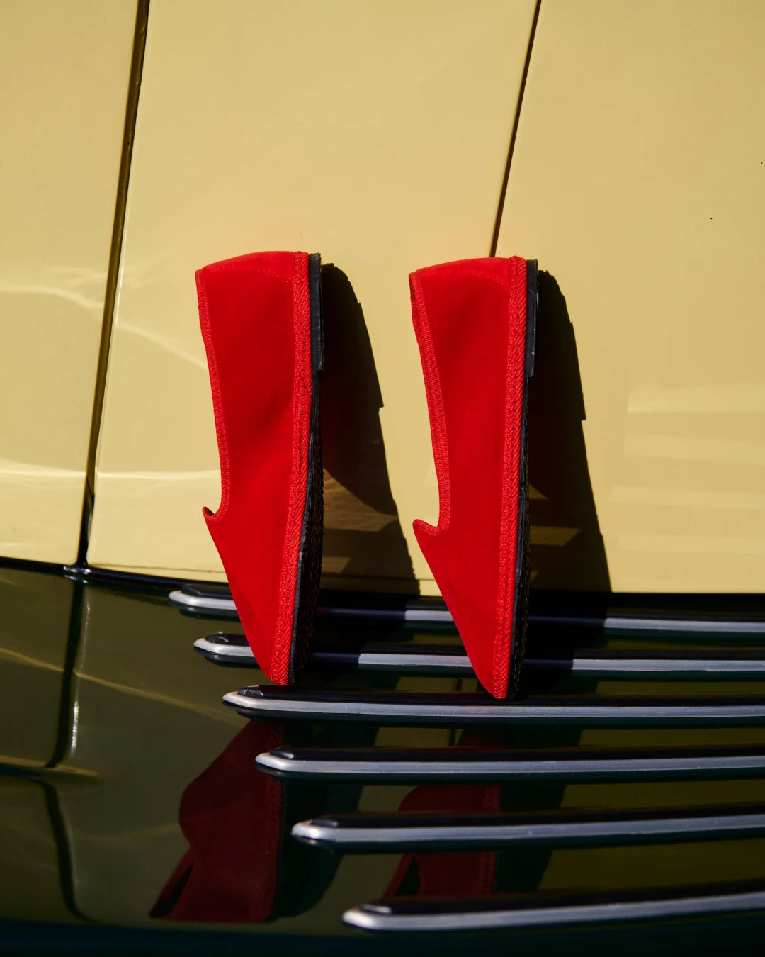 Red velvet friulane shoes photographed on a vintage car, showing the handcrafted Italian slipper silhouette.